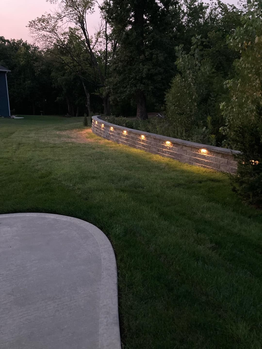Landscape with illuminated stone wall and green grass at dusk, enhancing outdoor ambiance.