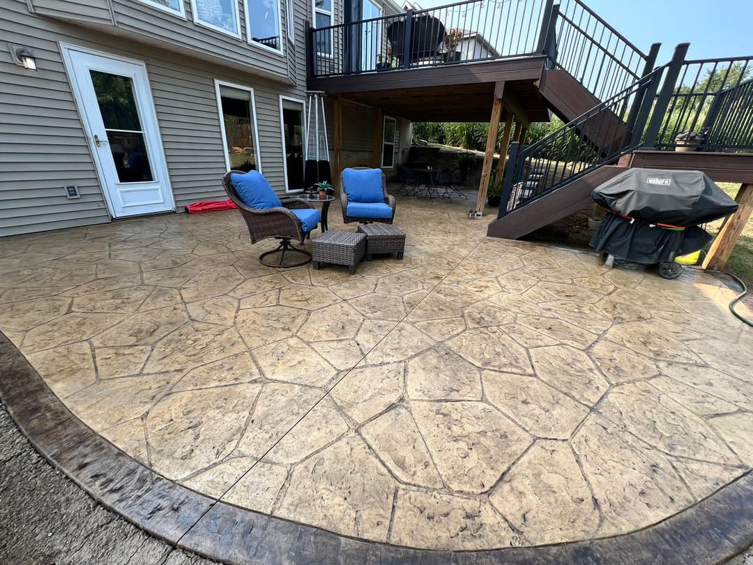 Stamped concrete patio with lounge chairs and grill, surrounded by a multi-level deck.
