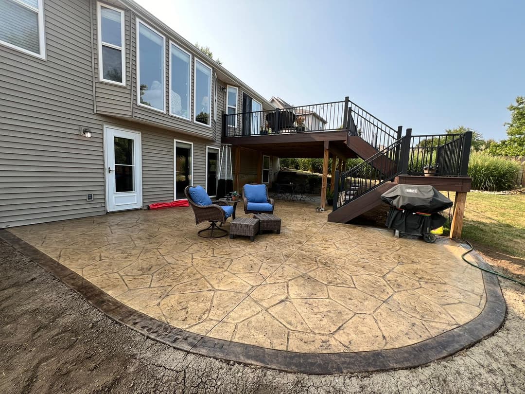 Backyard patio with stamped concrete, seating area, and stairs leading to upper deck.