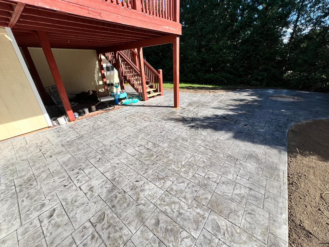Stamped concrete patio beside a wooden deck in a landscaped yard.