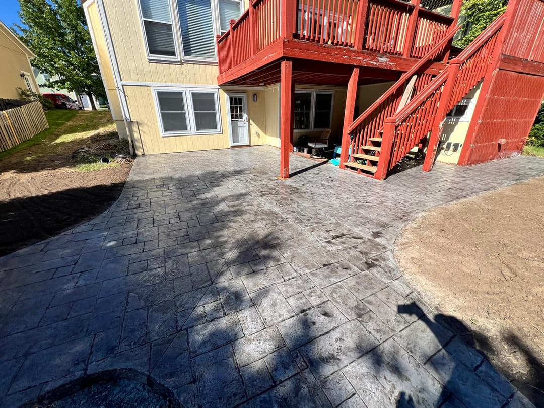 Stamped concrete patio with a red wooden deck and stairs at a residential home.