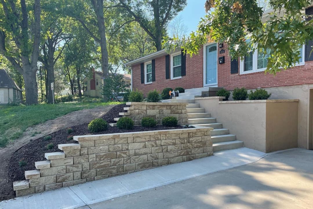 Modern home exterior with landscaped stairs, stone wall, and greenery under clear blue sky.
