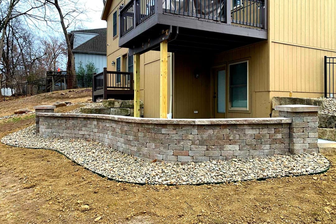 Stone retaining wall with gravel landscaping beside a modern home exterior.