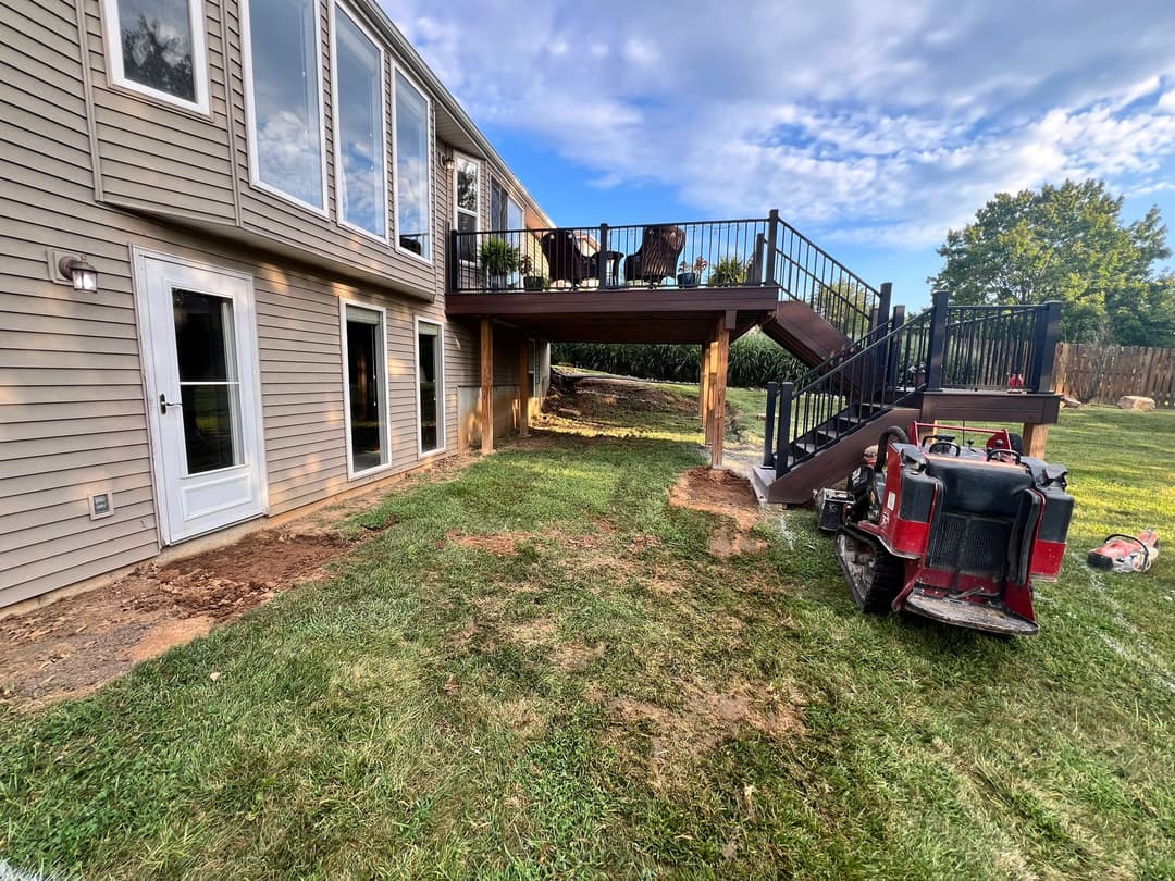 Backyard remodeling with elevated deck, green grass, and construction equipment nearby.