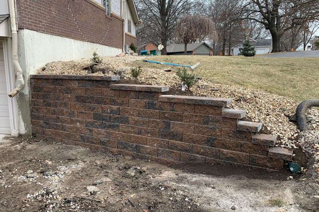 Retaining wall with steps made of stone, landscaped area with gravel and small plants.