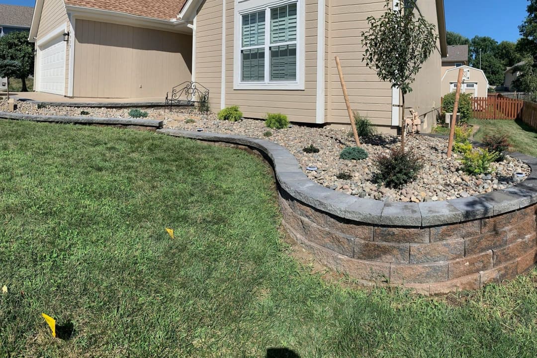 Landscaped garden with retaining wall, rocks, and plants next to a house.